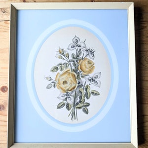 May include: A framed print of a bouquet of yellow roses and white flowers with green leaves. The print is set against a light blue background with a white oval border.