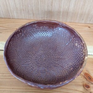 May include: A brown ceramic bowl with a textured, patterned surface. The bowl has a wide, round shape and a slightly flared rim.