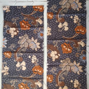 Może przedstawiać: Dwa kawałki tkaniny z ciemnoszarym tłem i wzorem kwiatowym w odcieniach pomarańczowego, brązowego i białego. Tkanina ma strzępiony brzeg.