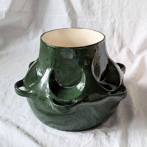 Puede incluir: Una olla de cerámica verde oscuro con una forma orgánica única y múltiples asas. La olla tiene un acabado liso y brillante y un interior blanco.