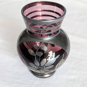 May include: A purple glass vase with silver floral designs and silver stripes around the rim.