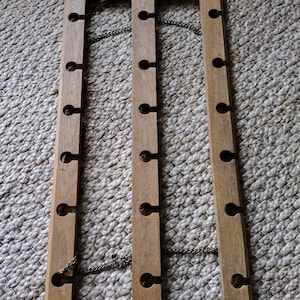 May include: Wooden wall-mounted rack with 12 holes for hanging items, featuring a chain detail.