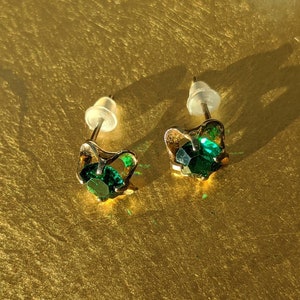 May include: A pair of gold earrings with green gemstone accents. The earrings have a simple, elegant design.