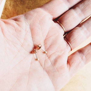 May include: A pair of gold stud earrings with small round balls on the ends.