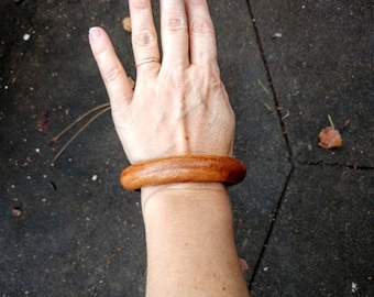 May include: A brown wooden bangle bracelet on a person's wrist.
