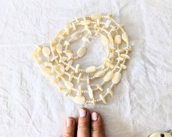 May include: A white pearl necklace with multiple strands of small pearls and larger, oval-shaped shell beads.