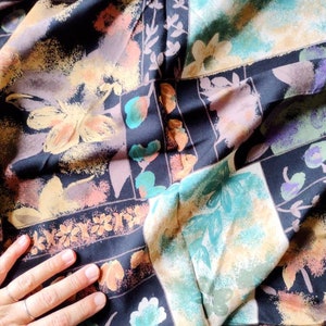 May include: A black fabric with a colorful floral pattern. The fabric has a patchwork design with different colored squares and rectangles. The flowers are in shades of yellow, orange, green, and blue.