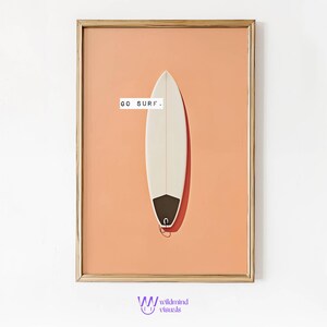 Puede incluir: Lámina enmarcada con una ilustración de una tabla de surf. La tabla es blanca con cola negra y un pequeño lazo. El fondo es color melocotón, y el texto "GO SURF" está encima. El marco es dorado.