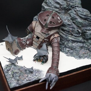 May include: A detailed model of a battle-damaged, brown and gray robot, partially embedded in a rocky terrain. The model features intricate details, including visible mechanical components and weathering effects. Gray bat-like figures are scattered around the robot.