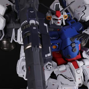 Puede incluir: Primer plano de un modelo mecha blanco, azul y rojo. El modelo presenta intrincados paneles, un arma grande y una cabeza detallada con detalles rojos. El dise&ntilde;o sugiere un tema futurista y rob&oacute;tico.