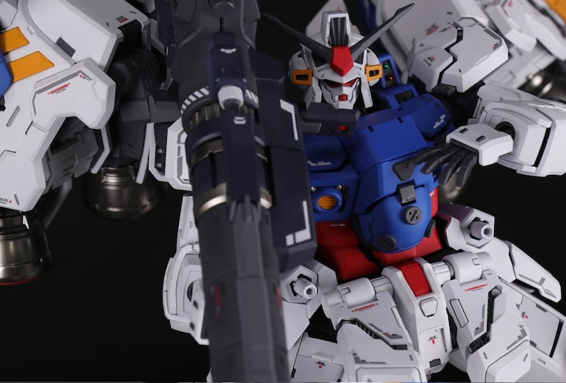 Puede incluir: Primer plano de un modelo mecha blanco, azul y rojo. El modelo presenta intrincados paneles, un arma grande y una cabeza detallada con detalles rojos. El dise&ntilde;o sugiere un tema futurista y rob&oacute;tico.