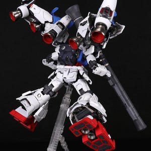 Puede incluir: Maqueta detallada y ensamblada de un robot mec&aacute;nico blanco y azul con detalles en rojo. El robot presenta m&uacute;ltiples propulsores, un arma grande y est&aacute; montado sobre un soporte transparente sobre un fondo negro. El modelo es muy detallado.