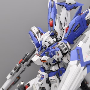 May include: A white and blue robot with multiple weapons and a large wingspan. The robot is posed in a dynamic stance with its arms extended.