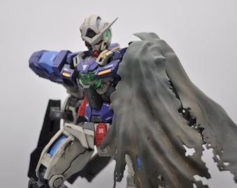May include: A blue and white robot action figure with a tattered gray cape. The robot has a green visor and a detailed design.