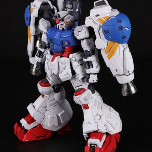 Puede incluir: Modelo detallado de un robot Gundam, principalmente blanco con detalles azules, rojos y amarillos. El robot tiene un dise&ntilde;o complejo con articulaciones, un pecho azul y grandes protectores de hombros. Los pies y las piernas inferiores son rojos.
