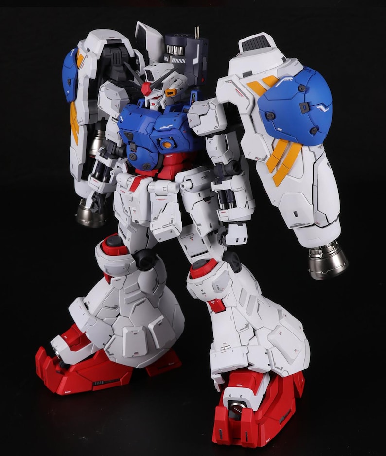 Puede incluir: Modelo detallado de un robot Gundam, principalmente blanco con detalles azules, rojos y amarillos. El robot tiene un dise&ntilde;o complejo con articulaciones, un pecho azul y grandes protectores de hombros. Los pies y las piernas inferiores son rojos.
