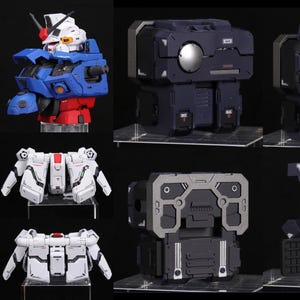 Puede incluir: Colecci&oacute;n de kits de modelos detallados, incluyendo cabezas de robots en azul, rojo y blanco, y varios componentes mec&aacute;nicos en blanco, gris y negro. Los kits se exhiben sobre soportes transparentes.