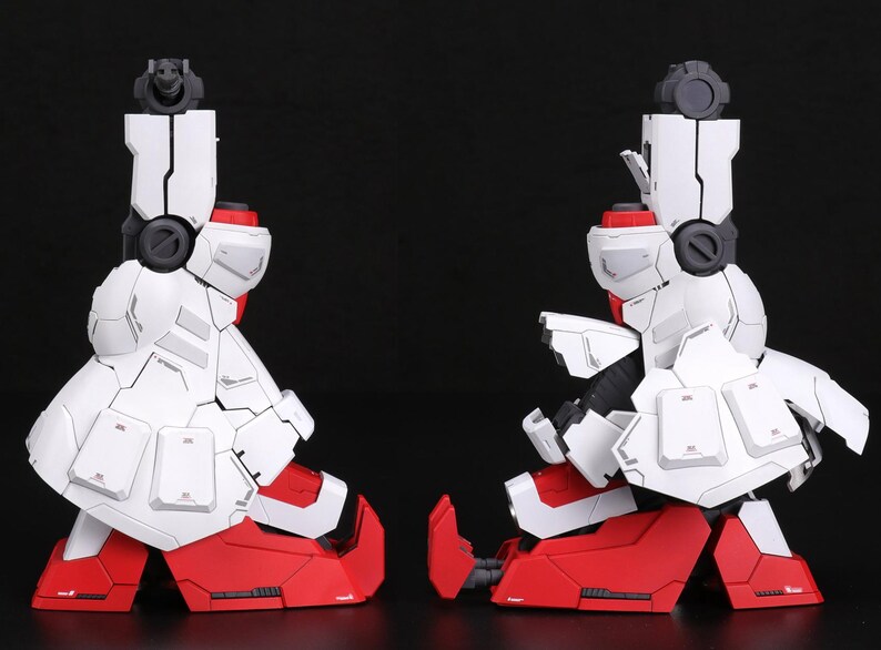 Puede incluir: Dos componentes de piernas rob&oacute;ticas blancas y rojas, posiblemente de un kit de modelo, se colocan uno al lado del otro sobre un fondo negro. Los componentes presentan paneles y detalles intrincados, con detalles en rojo en los pies y las articulaciones.