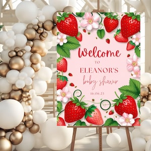 May include: Welcome to Eleanor's Baby Shower sign with a pink background and a strawberry theme. The sign features red strawberries, green leaves, and pink flowers. The text on the sign reads "Welcome to Eleanor's Baby Shower 16.06.23".