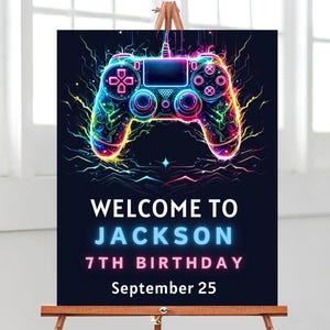 Op de afbeelding: Een neonblauw en roze welkomsbord met een gloeiende afbeelding van een videogamecontroller. Het bord zegt "Welkom bij Jackson 7e verjaardag September 25".
