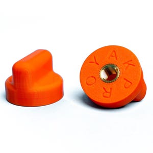 May include: Two bright orange knobs with a textured surface are displayed against a white background. One knob is cylindrical with a rectangular top. The other is circular with the letters "RO Y A K P" around a central brass fitting.