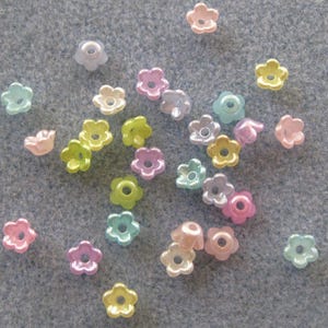May include: A collection of small, flower-shaped beads in various pastel colors, including pink, yellow, green, and blue. The beads have a glossy finish and a hole in the center, suitable for jewelry making or crafts.