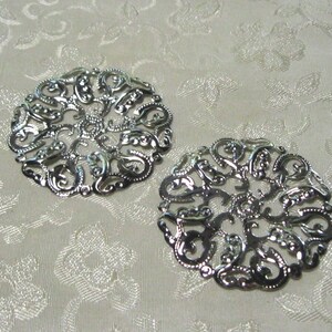 May include: Two silver filigree metal embellishments with a circular design. The embellishments have a delicate, intricate pattern.