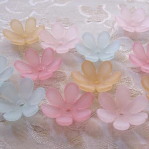 May include: A collection of translucent flower-shaped beads in various pastel colors, including pink, peach, yellow, and light blue. The beads have five petals and a small hole in the center, suggesting they are for crafting or jewelry making.