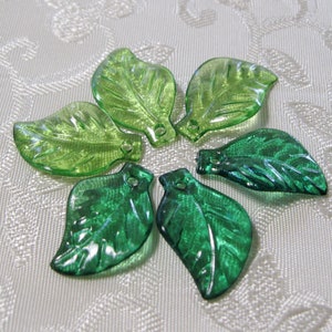 May include: Six green glass leaf charms with a hole at the top for hanging. The leaves are in two shades of green, a lighter green and a darker green.