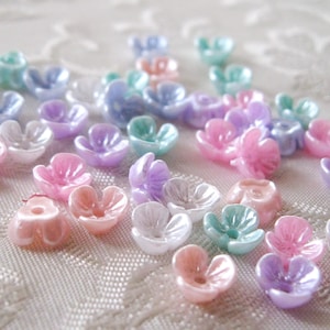 May include: Assortment of pastel colored plastic flower beads. The beads are in shades of pink, purple, blue, and green. They are all in the shape of a flower with five petals.
