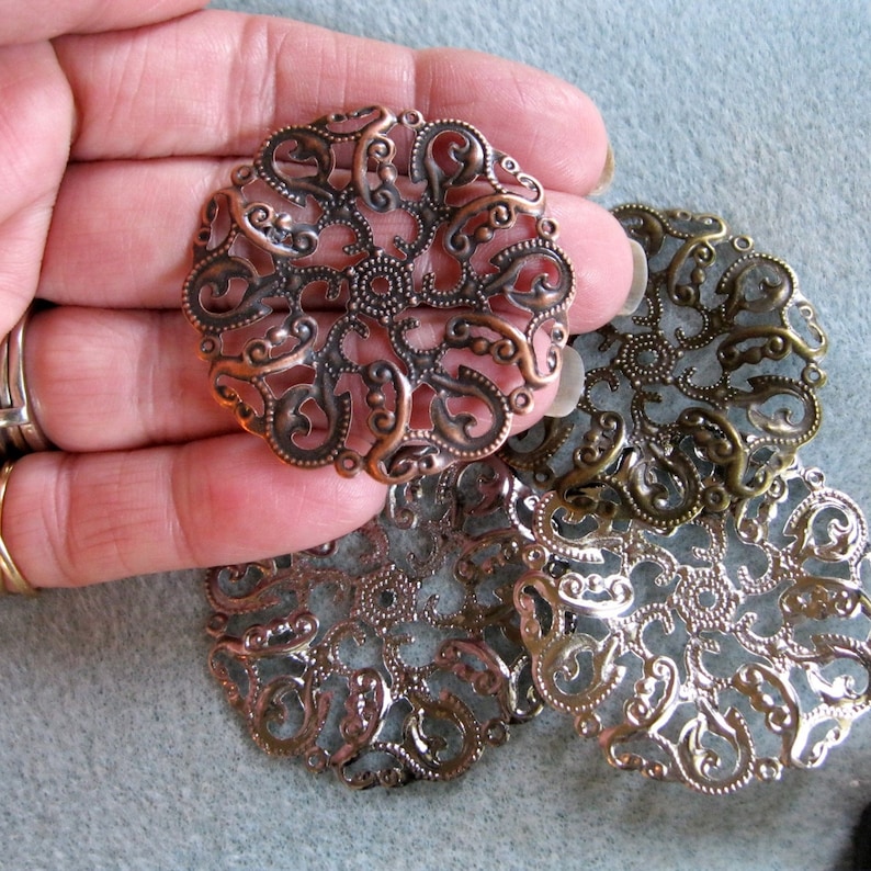 May include: Four decorative metal filigree embellishments in copper, brass, and silver tones. The filigree is in a circular shape with a delicate, intricate design.