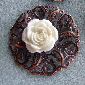May include: A white ceramic rose with a detailed design sits in the center of a copper filigree embellishment.