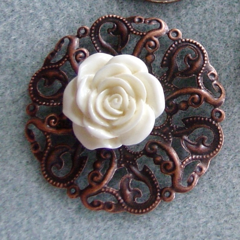 May include: A white ceramic rose with a detailed design sits in the center of a copper filigree embellishment.