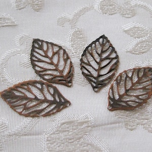 May include: Four copper leaf-shaped metal charms with a delicate, intricate design. The leaves are cut out and have a slightly distressed finish.