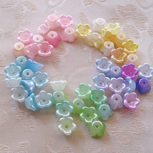 May include: A collection of translucent flower-shaped beads in a variety of pastel colors, including pink, blue, green, yellow, and purple. The beads are arranged in a circular pattern, showcasing their delicate design and subtle color variations.