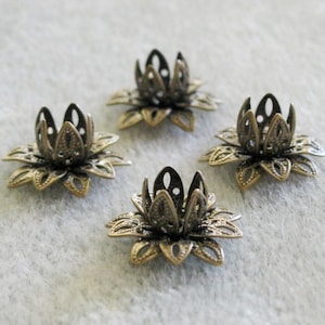 May include: Four antique gold-toned metal lotus flower bead caps. Each cap has a delicate, intricate design with a hollow center.