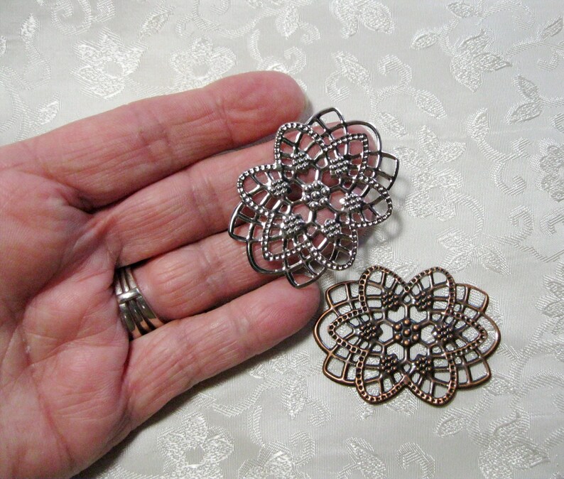 K&ouml;nnte beinhalten: Zwei filigranartige Verzierungen aus Metall, eine silberfarben und eine kupferfarben, mit einem detaillierten geometrischen Muster.