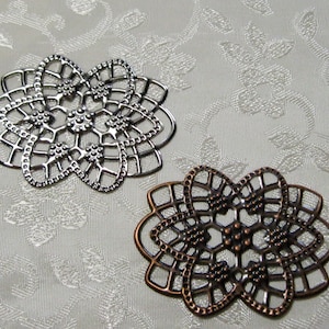 K&ouml;nnte beinhalten: Zwei dekorative filigranartige Metallst&uuml;cke, eines silberfarben und eines kupferfarben, mit einem floralen Design. Die St&uuml;cke sind filigran und detailliert, mit einem zarten Muster aus Kreisen und Linien.