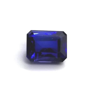 Puede incluir: Una gema rectangular de color azul oscuro con talla esmeralda. La gema se encuentra sobre un fondo blanco, mostrando sus facetas y su rico color. Ideal para la creación de joyas.