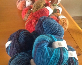 May include: A collection of yarn skeins in various colours, including orange, red, blue, and brown. The yarn is arranged in a line on a wooden surface.