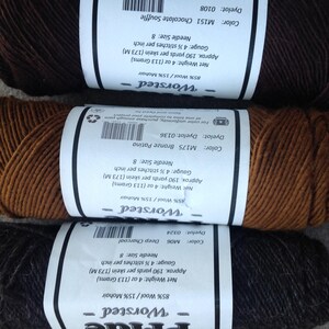 May include: Three skeins of worsted weight yarn in shades of brown and charcoal. Each skein has a label with details including color, dye lot, and fiber content of 85% wool and 15% mohair. The labels also indicate the weight is 4 oz (113 grams).