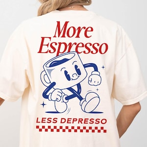 Könnte beinhalten: Cremefarbenes T-Shirt mit den roten Worten "More Espresso" über einer Cartoon-Kaffeetasse. Darunter steht in Rot der Text "LESS DEPRESSO", über einem rot-weiß karierten Muster.