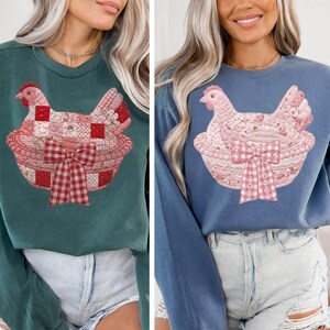 以下が含まれることがあります： 長袖スウェットシャツ2枚。1枚はティール、もう1枚はブルーで、それぞれバスケットに入った鶏の詳細なグラフィックが特徴です。鶏とバスケットはパッチワーク模様とギンガムリボンで装飾されています。スウェットシャツはカジュアルで快適です。