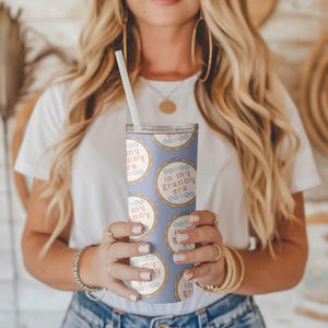 Puede incluir: Un vaso azul claro con una pajita blanca, con un patr&oacute;n repetido de dise&ntilde;os circulares con el texto "in my granny era" en rojo. El vaso es sostenido por una persona.