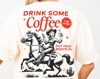 May include: A white t-shirt with a black and white illustration of a woman riding a horse. The text "Drink Some Coffee" is in red with a red star and the text "Yee-Haw!" in a red circle. The text "Put Your Boots On" and "Handle Your Shit" are also in red.