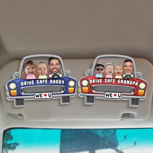 May include: Two car-shaped visor ornaments. One is blue with the text "DRIVE SAFE DADDY" and "WE U" with a picture of a man and two babies. The other is red with "DRIVE SAFE GRANDPA" and "WE U" with a picture of a man and three babies.