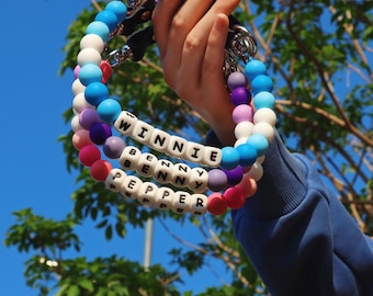 May include: Three colorful beaded bracelets with the names "Winnie", "Benny", and "Pepper" spelled out in white letters. The bracelets are made of silicone beads in shades of blue, purple, pink, and white.