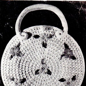 May include: A white crocheted handbag with a round shape and a handle. The bag has a floral design with dark brown accents.