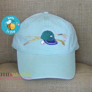 May include: A light blue baseball cap with an embroidered design of a golf club, golf ball, and a green and blue golf hat.