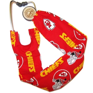 May include: Red stethoscope cover with a Kansas City Chiefs logo and the word "Chiefs" repeated multiple times. The cover is made of fabric and has a yellow and white color scheme.